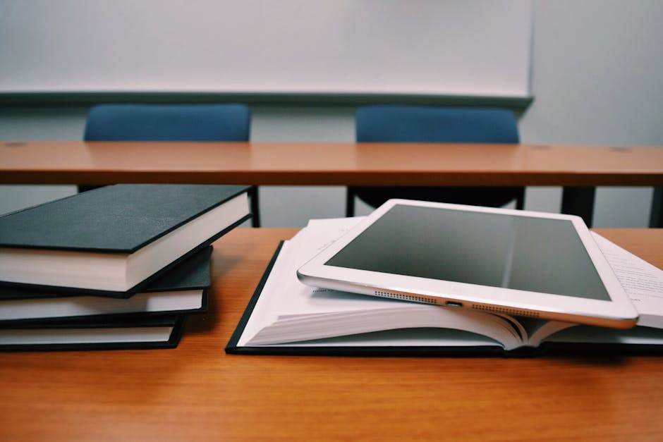 Books and a tablet on a desk in a classroom, depicting modern education