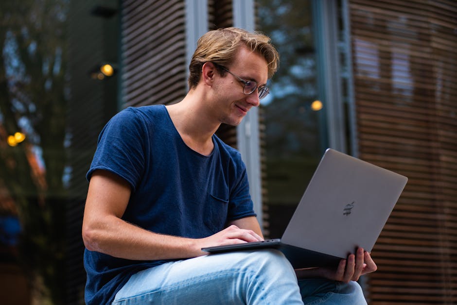 A young man sitting outdoors in Leiden, Netherlands, working on a laptop